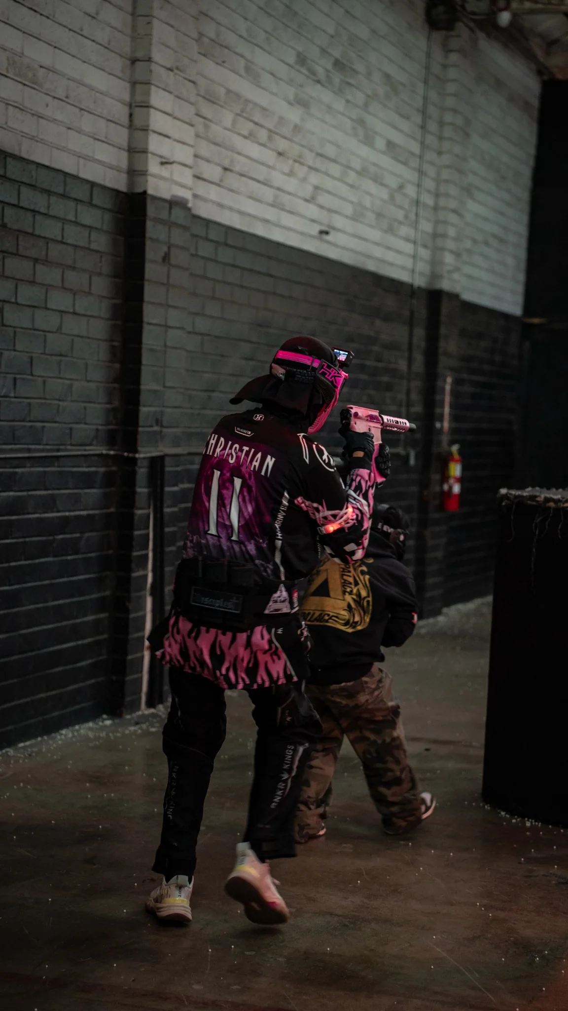 Disciples Airsoft player moving through an indoor field in a custom black and pink jersey
